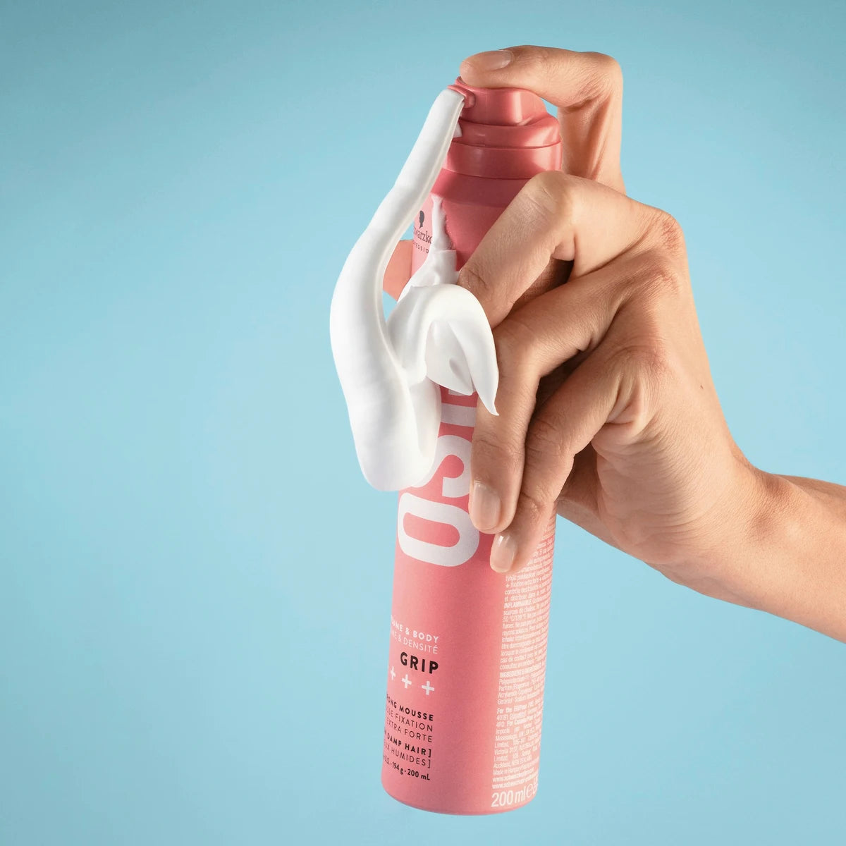 Hand holding a pink bottle with a white nozzle against a light blue background