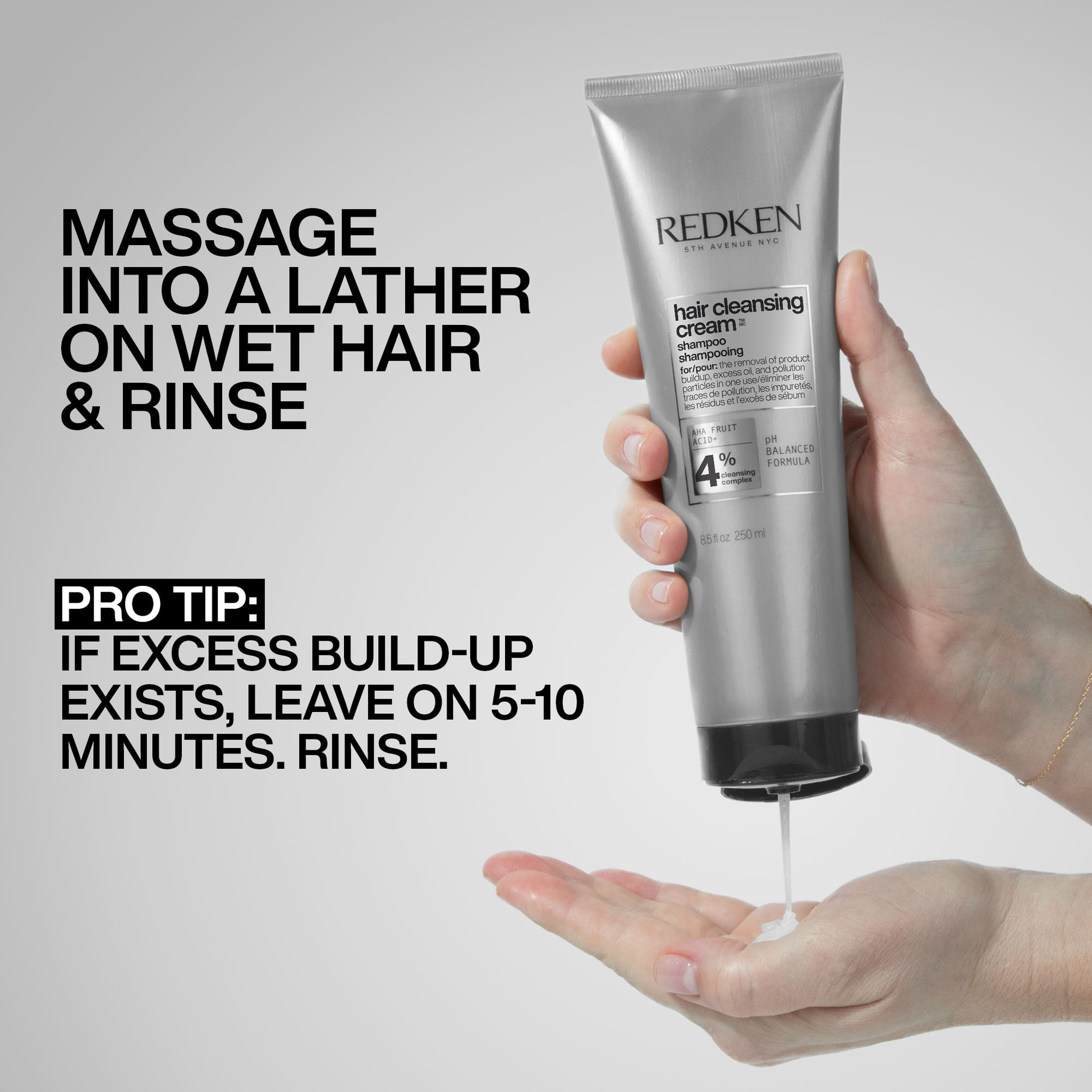 Redken hair cleansing cream tube with hand holding it and showing cream on palm, on a gray background.