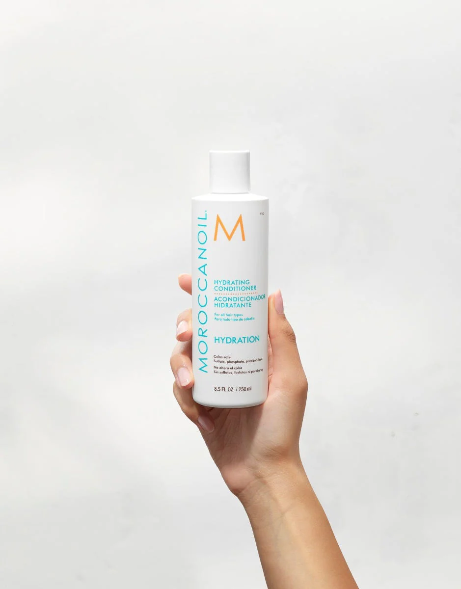 Hand holding a Moroccanoil bottle against a white background