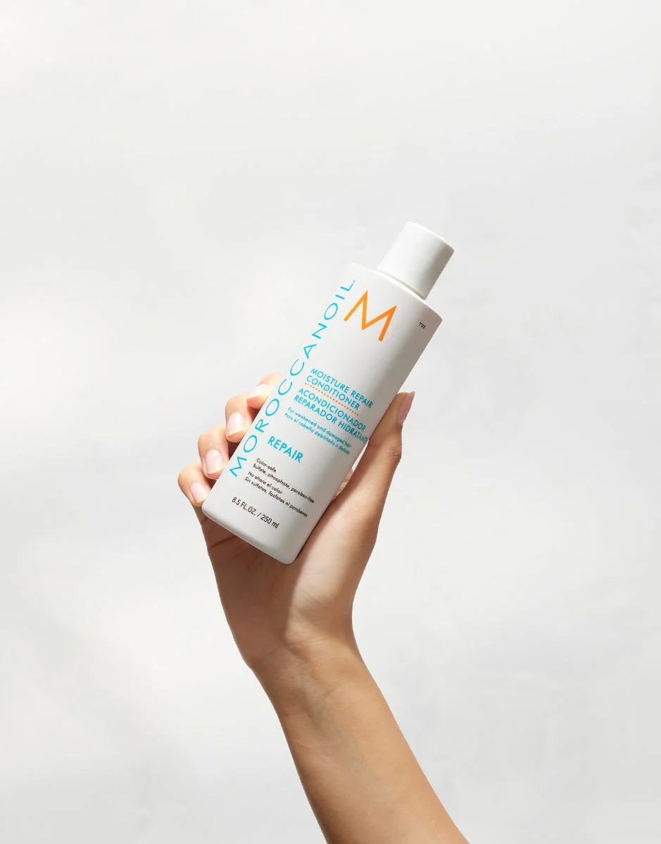 Hand holding a bottle of Moroccanoil product against a light gray background