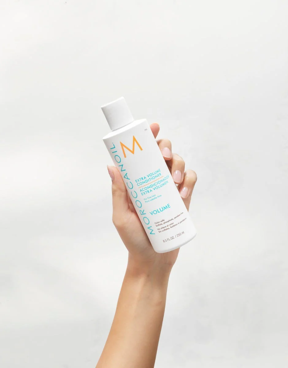 Hand holding a bottle of Moraccanoil volumizing shampoo against a white background