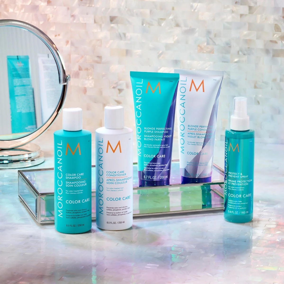Moroccanoil hair care products on a reflective surface with a mirror in the background.