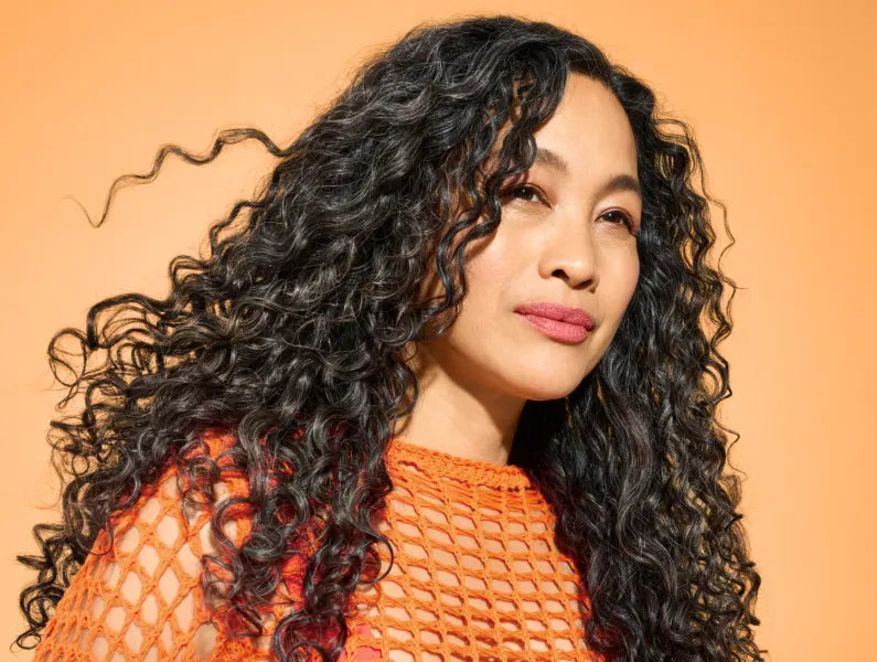 Woman with curly hair wearing an orange top against an orange background