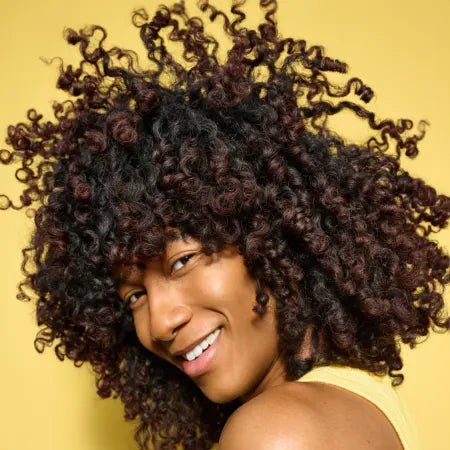 Woman with curly hair smiling against a yellow background