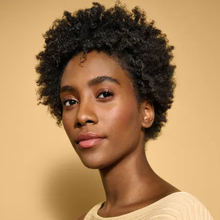 Woman with short, curly hair wearing a beige sweater against a beige background