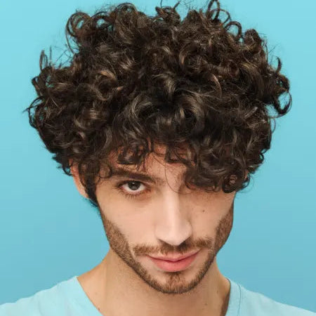 Man with curly hair wearing a light blue sleeveless shirt against a blue background