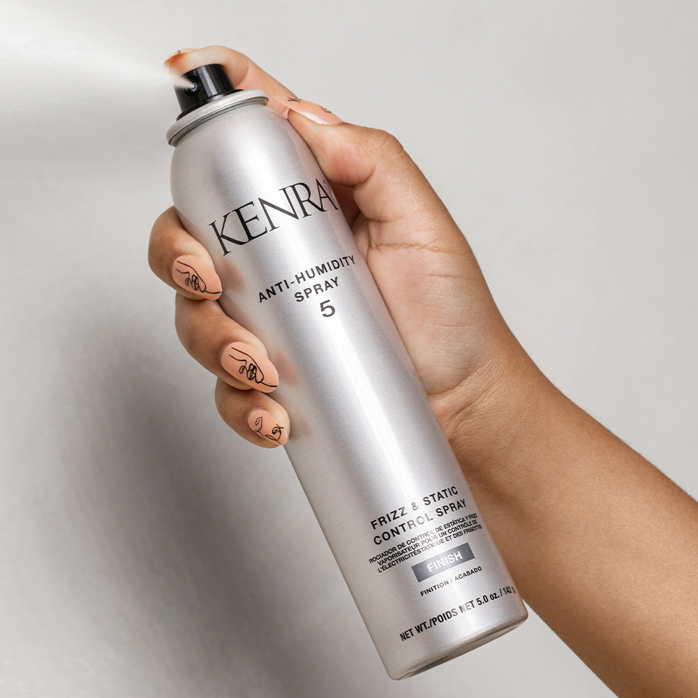 Hand holding a can of Kenra Anti-Humidity Spray against a neutral background