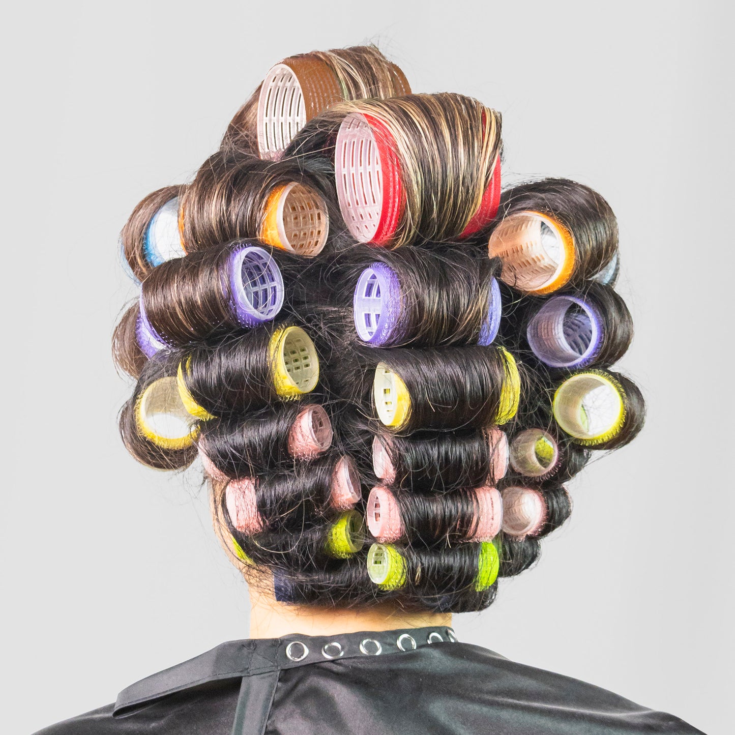 Person with hair in colorful rollers on a plain background