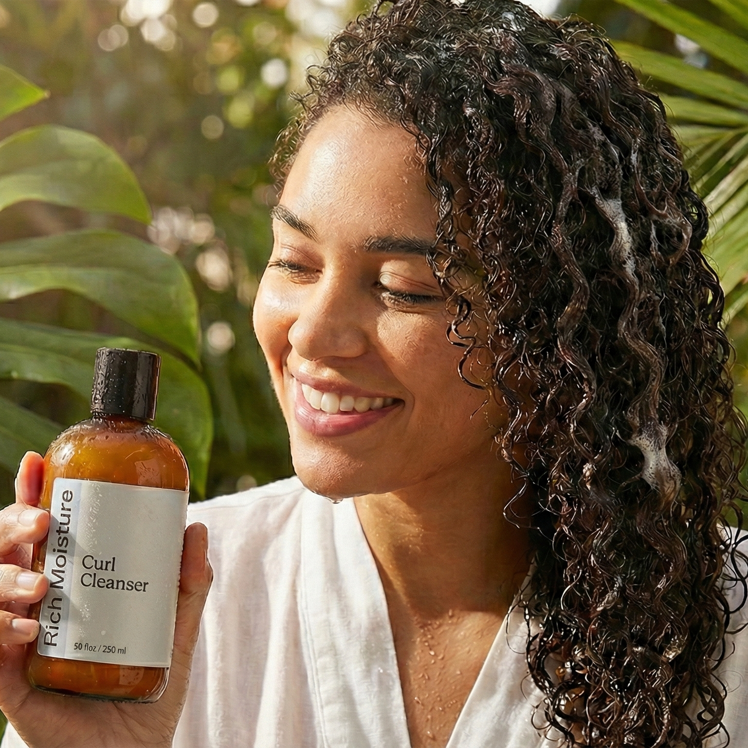Woman holding a bottle of hair care product with green foliage in the background