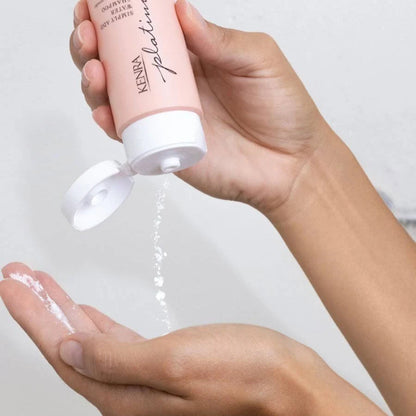 Hand holding a Kenra Platinum hair product with white powder being applied to another hand.