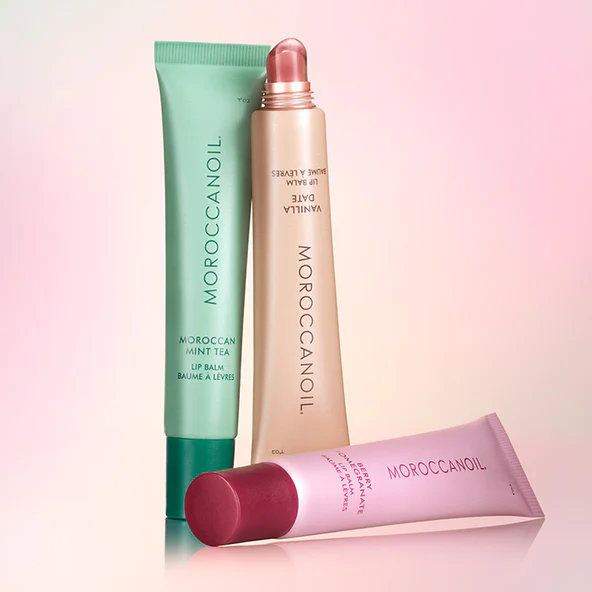 Three Moroccanoil lip balms on a gradient pink and green background
