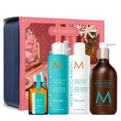Moroccanoil The Volume Suite gift set featuring a pink and navy blue gift box, three volumizing haircare bottles (shampoo, conditioner, and light oil) in turquoise and white, and a body lotion bottle in dark brown, arranged on a white background.