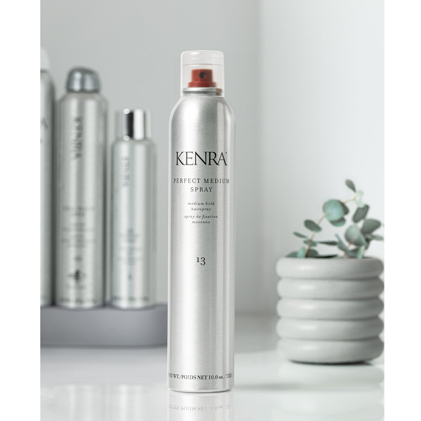 Kenra hair spray bottle on a white surface with a plant in the background