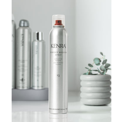 Kenra hair spray bottle on a white surface with a plant in the background