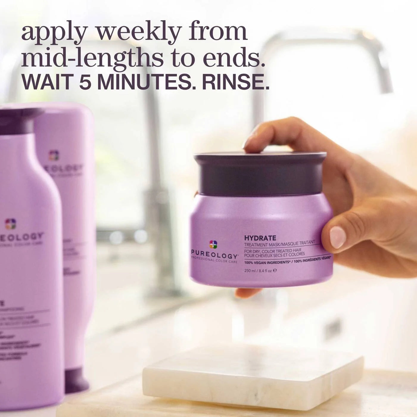 Hand holding a purple hair treatment jar with product bottles in the background