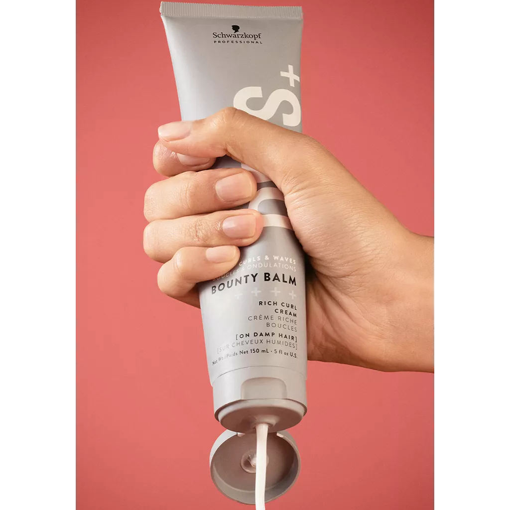 Hand holding a tube of Schwarzkopf Bounty Balm against a red background