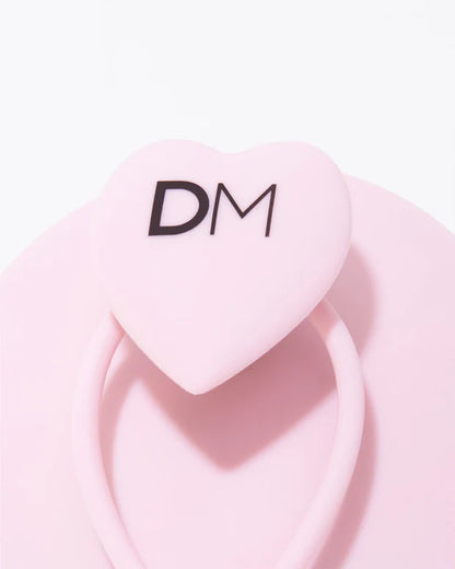 Pink heart-shaped container with 'DM' logo on a light pink background