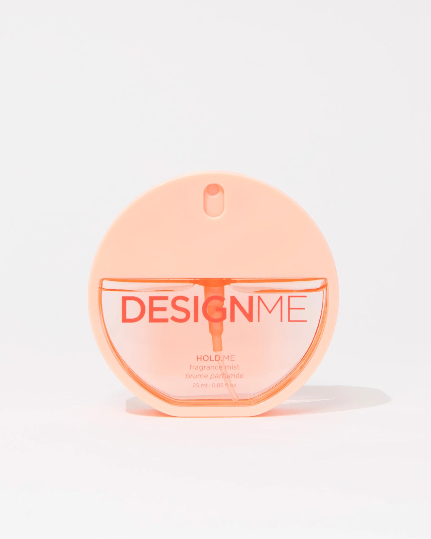 A round, translucent peach-colored perfume bottle labeled 'DESIGNME HOLD ME' on a clean white background.