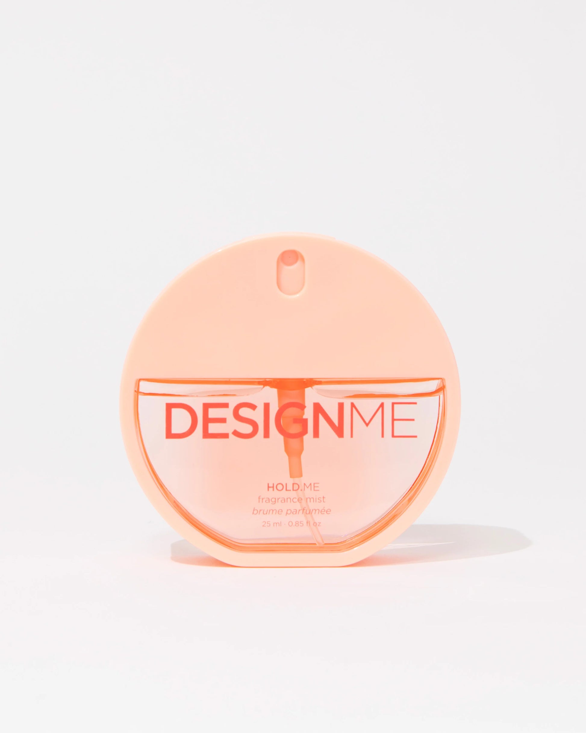 A round, translucent peach-colored perfume bottle labeled 'DESIGNME HOLD ME' on a clean white background.