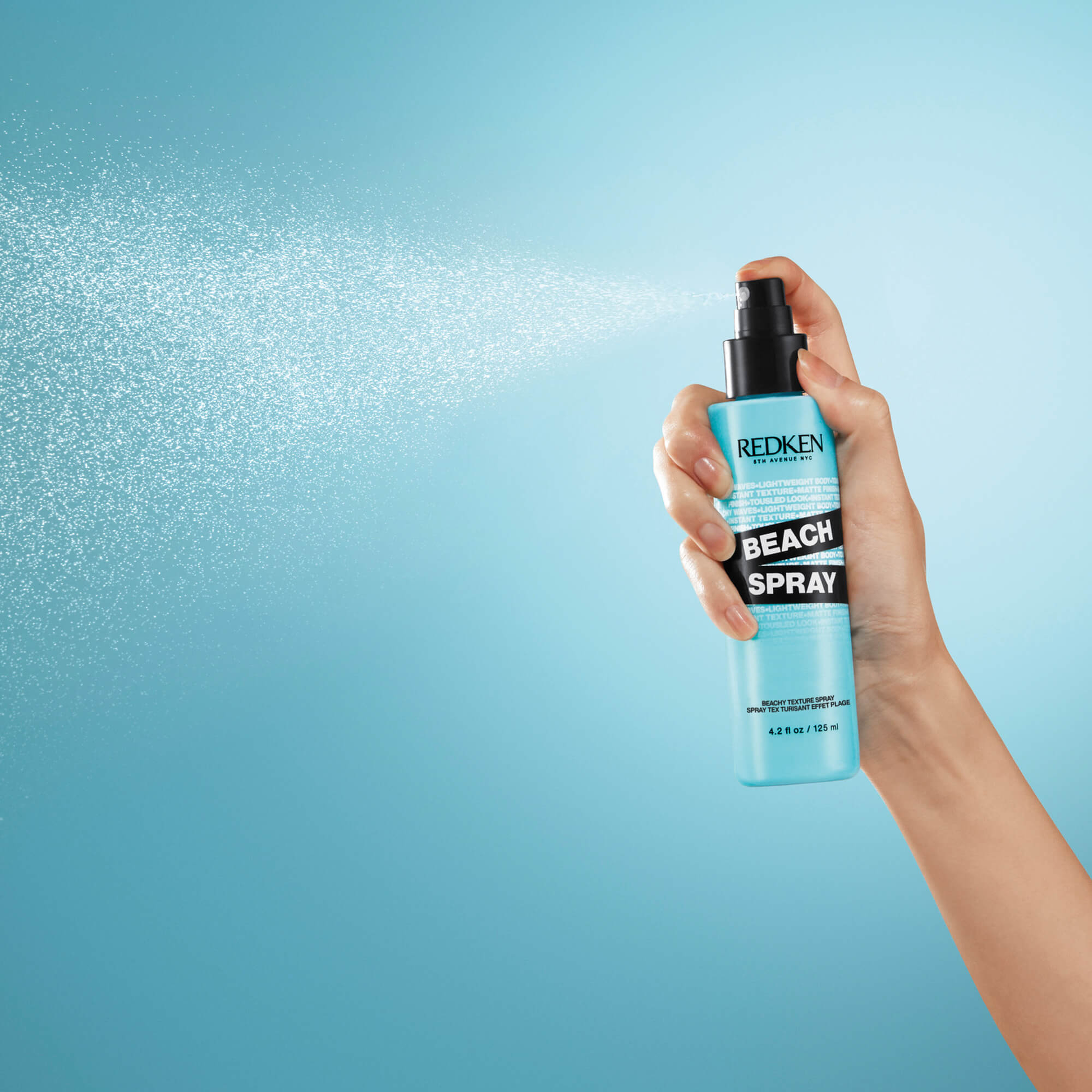 Hand holding a Redken Beach Spray bottle with a blue background