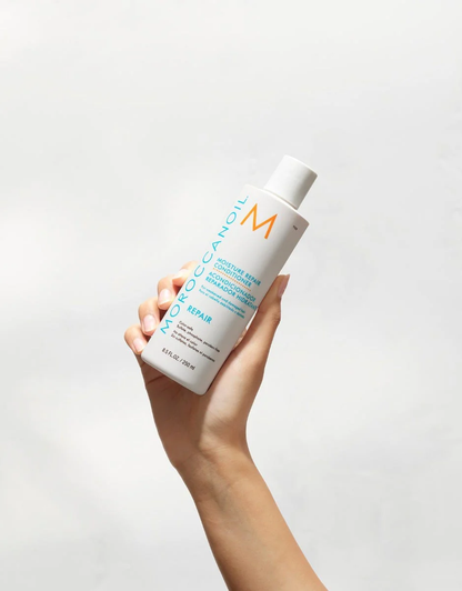 Hand holding a bottle of Moroccanoil product against a light gray background