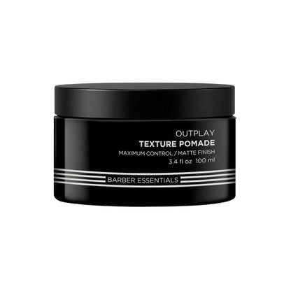 A black plastic jar of Outplay Texture Pomade by Barber Essentials, featuring white text and silver stripes on the front label, set against a plain white background.
