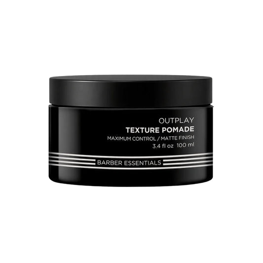 A black plastic jar of Outplay Texture Pomade by Barber Essentials, featuring white text and silver stripes on the front label, set against a plain white background.